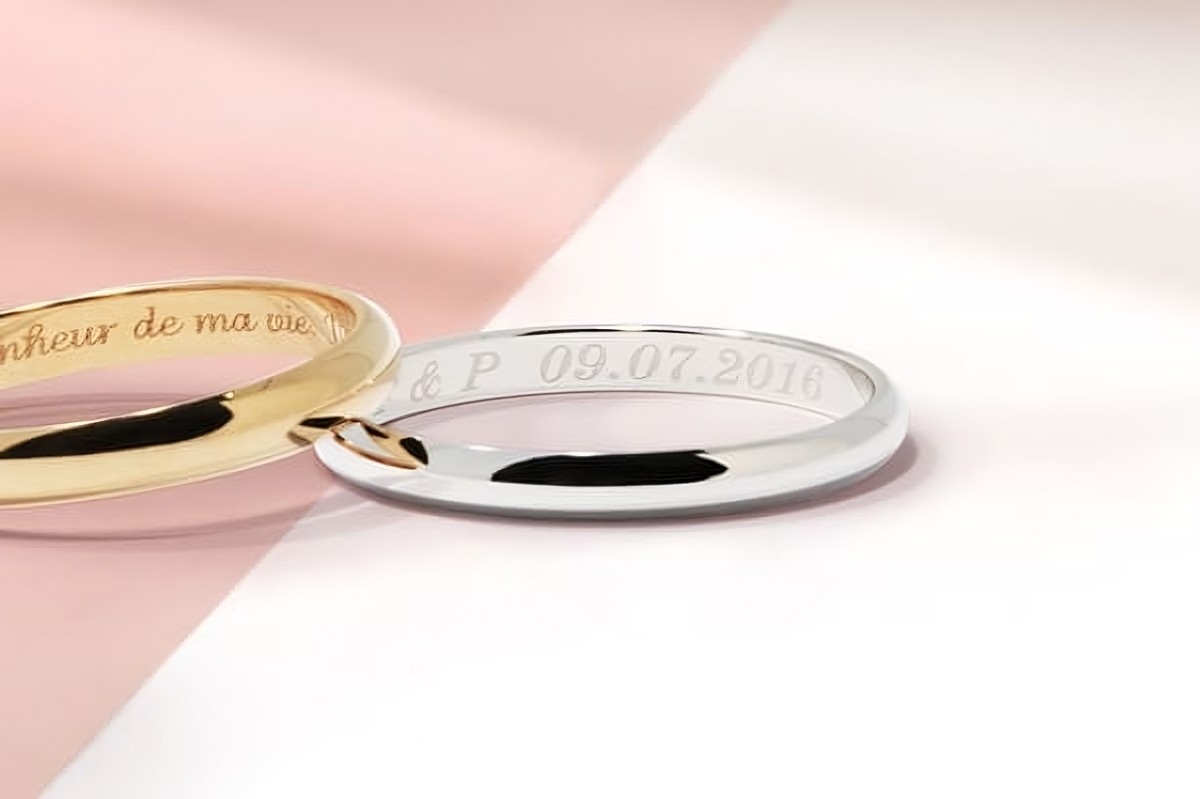 Deux alliances gravées, l’une en or jaune avec un message romantique, l’autre en or blanc avec des initiales et une date, symbole d’un amour éternel.